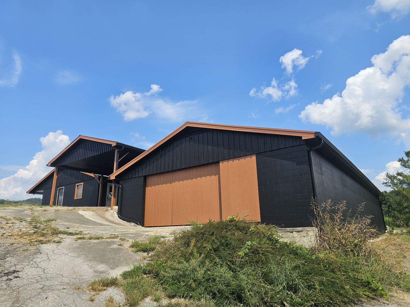 Barns painted black with copper-colored doors under a blue sky.